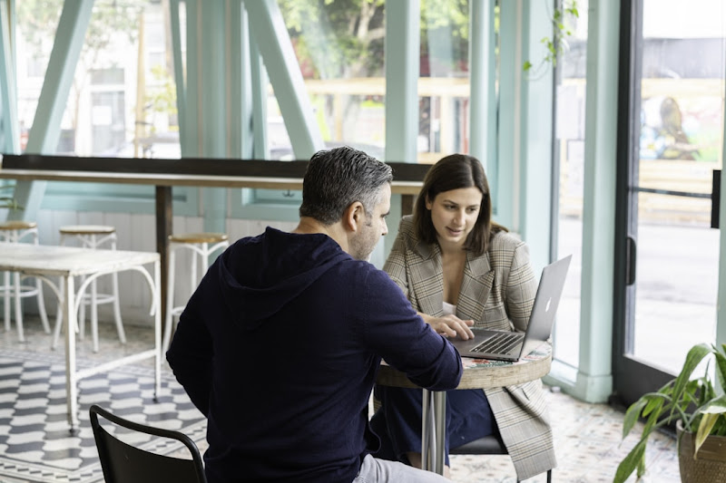 A man and woman collaborate at a table, using a laptop to discuss the proposal tool's impact on sales efficiency.